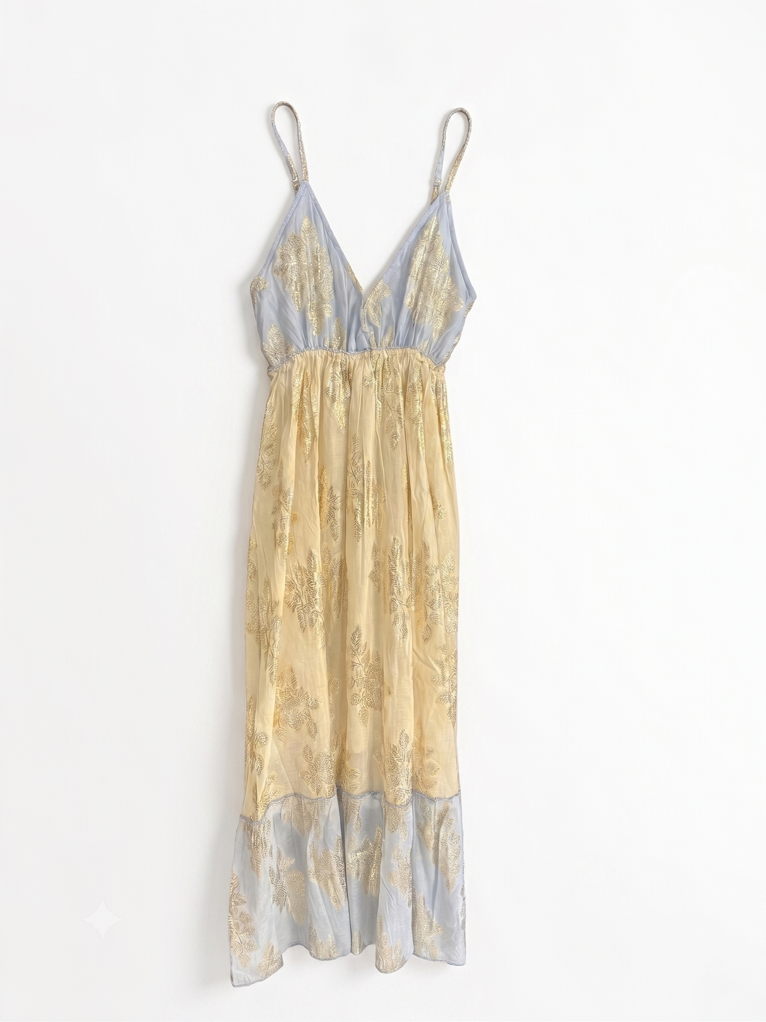A sleeveless, V-neck sheer dress with thin straps, featuring a pleated beige and gold patterned skirt and light blue ruffled trim at the hem and shoulders, laid flat on a white background.